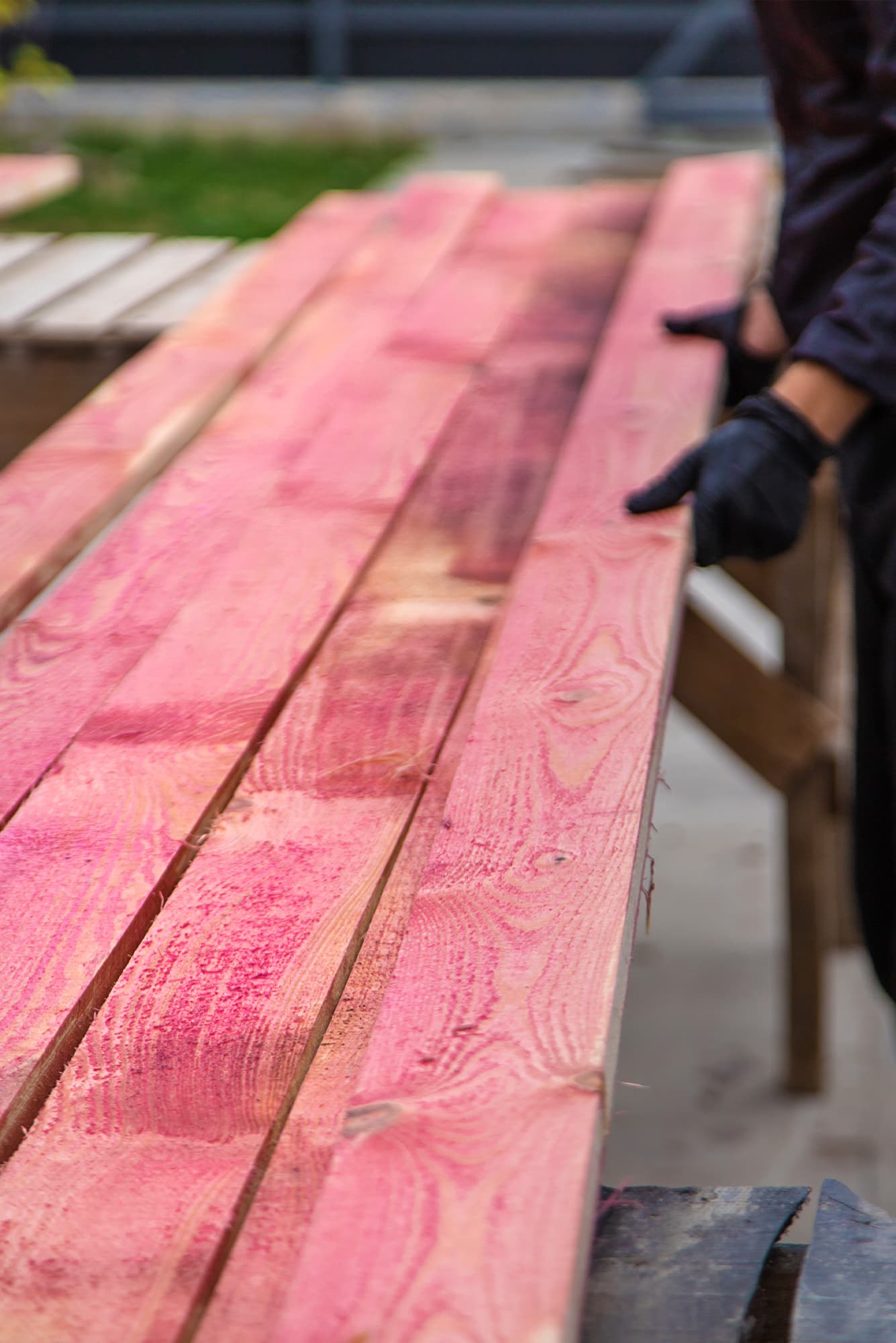 Zbliżenie na długie belki więźby dachowej poddane impregnacji zanurzeniowej na czerwono, przygotowane do montażu konstrukcji dachu.