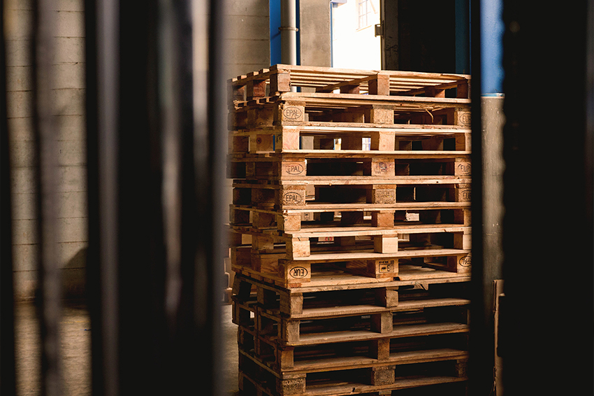 Wysokie stosy gotowych palet drewnianych z widocznymi oznaczeniami EPAL, ułożone w ciemniejszym pomieszczeniu magazynowym.
