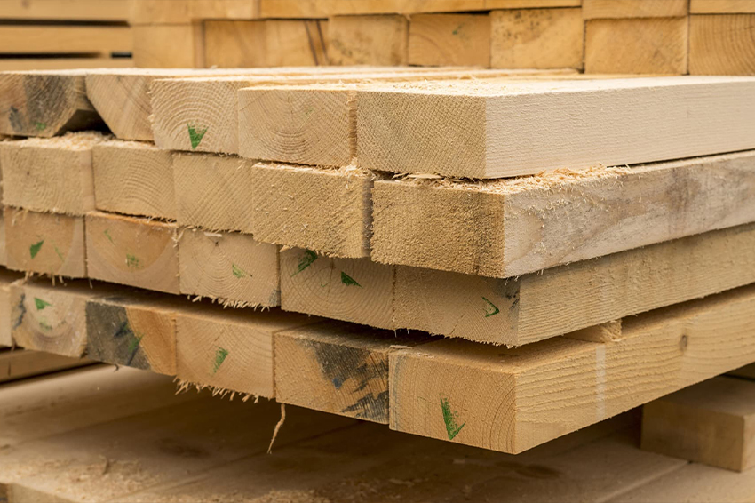 Zbliżenie na czoła równo ułożonych desek paletowych w sztaplu, z widocznymi zielonymi oznaczeniami klasyfikacji drewna.