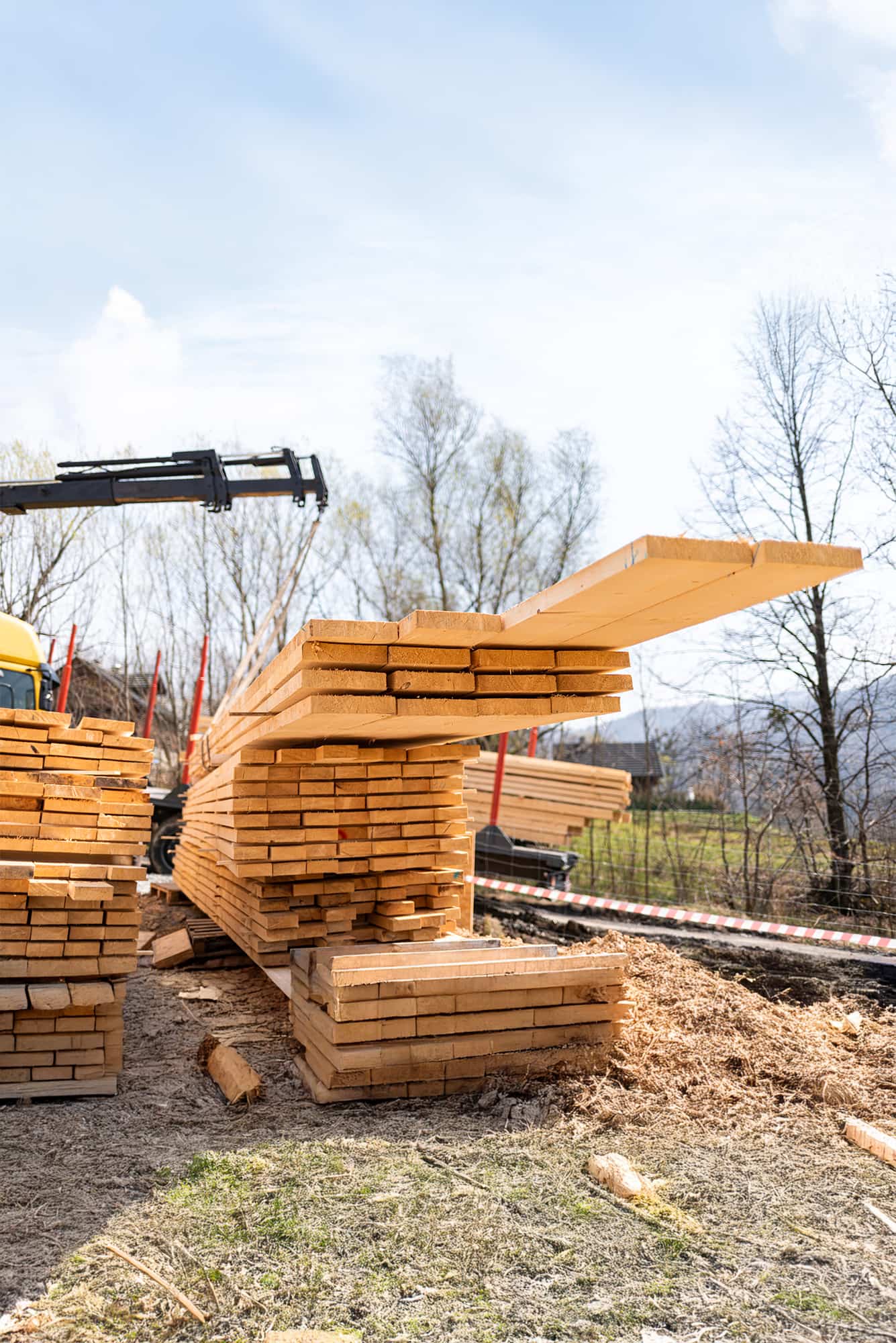 Samochód ciężarowy z dźwigiem HDS ładujący długie deski tarcicy iglastej na placu składowym tartaku.
